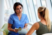 Patient with blonde hair meeting with female medical practitioner wearing blue scrubs